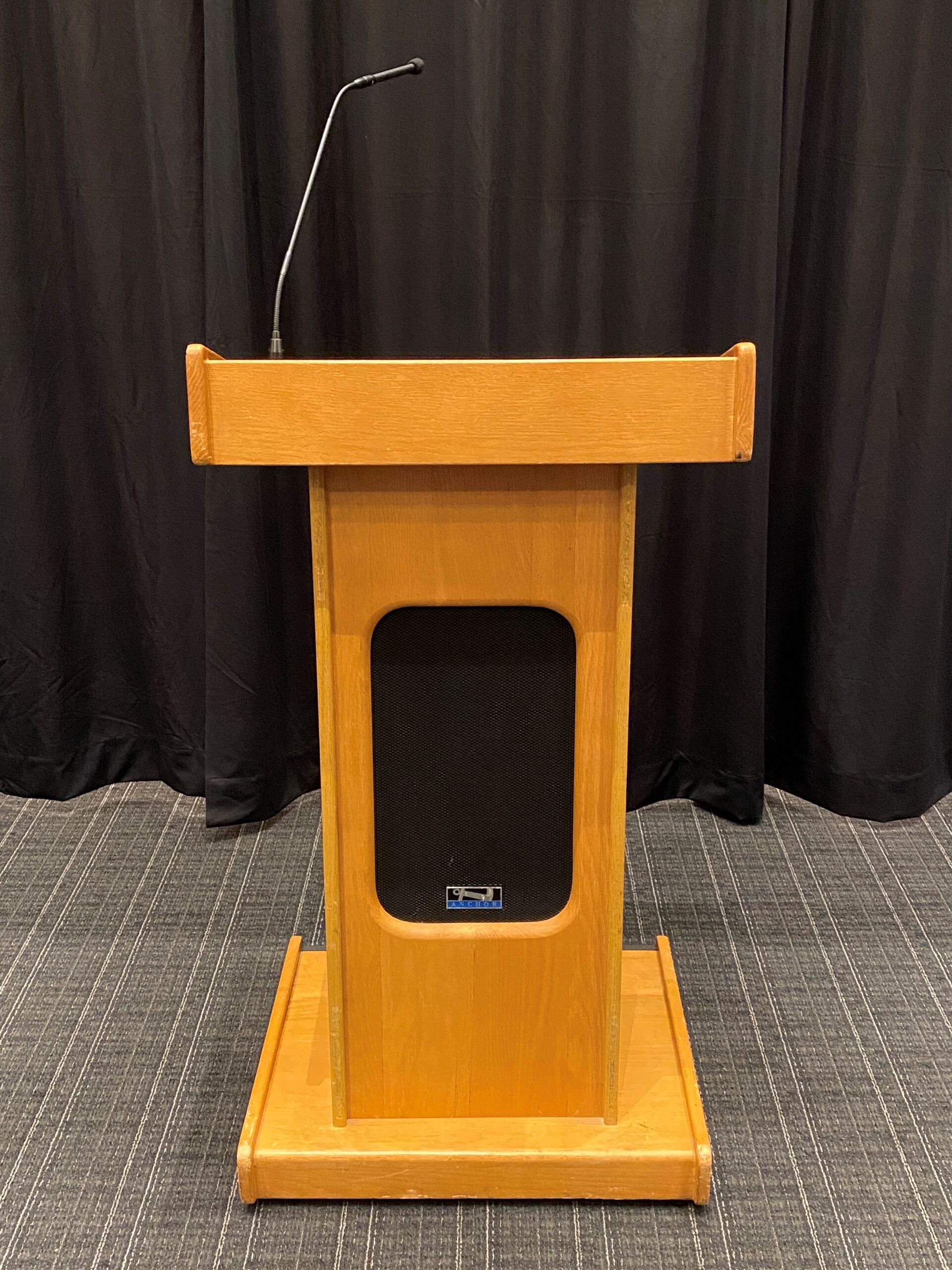 A wooden standing-height mobile lectern with a gooseneck microphone.